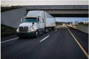 A white tractor-trailer driving on the highway passing under a bridge.