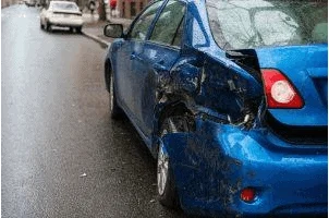 Blue car parked on a street, with severe rear-end damage.