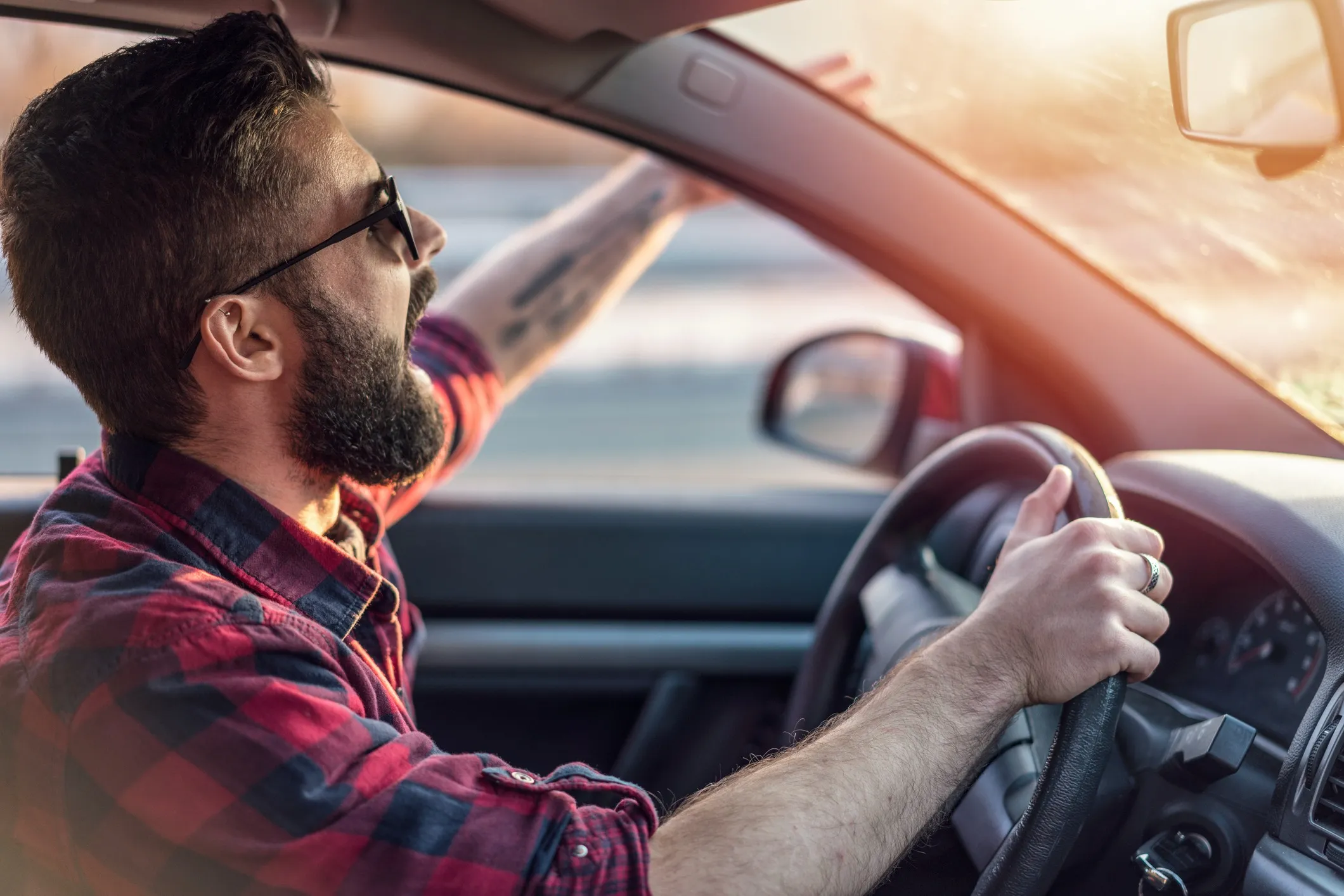 A angry male driver with a beard and his hand out of the window, shouting.