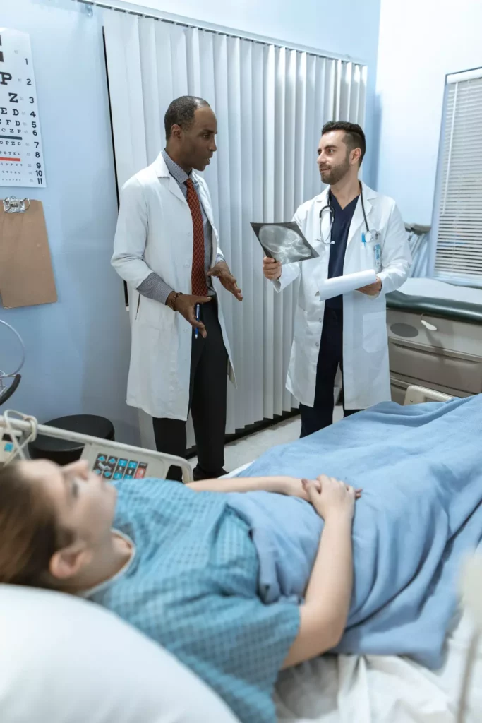 Two doctors looking at an x-ray with a patient in bed.