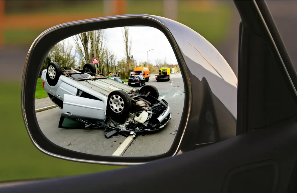 A car flipped over shown in a side mirror.