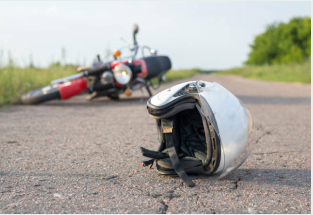 A motorcycle laying on the side of a road and a helmet on the ground.