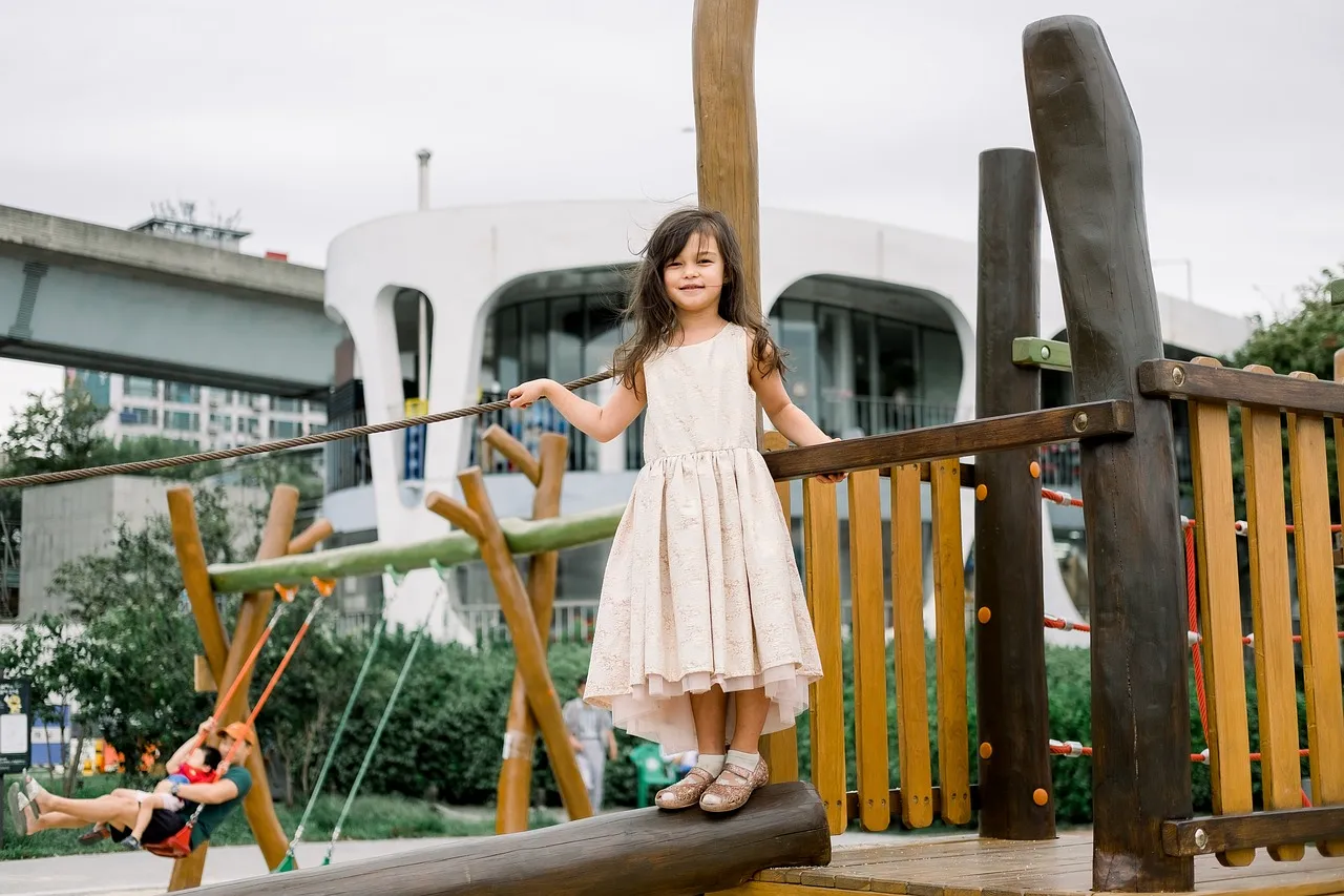 A child smiling while standing on a playground set.