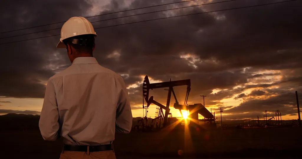 A worker in a hard hat outside of an oil rig.
