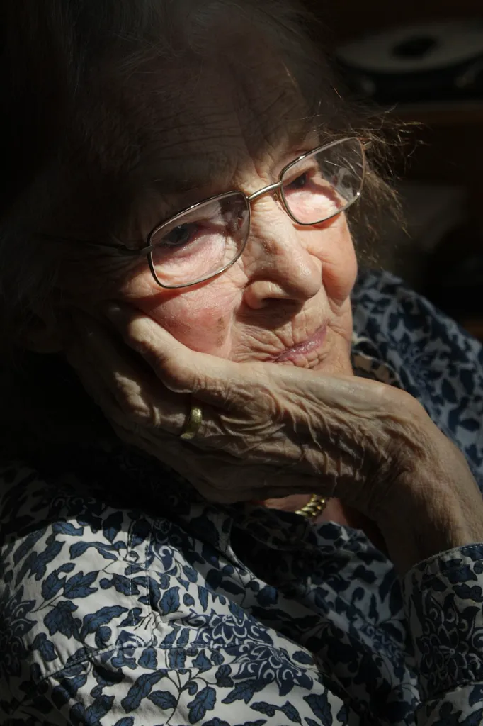 An elder woman, looking sadly out a window.