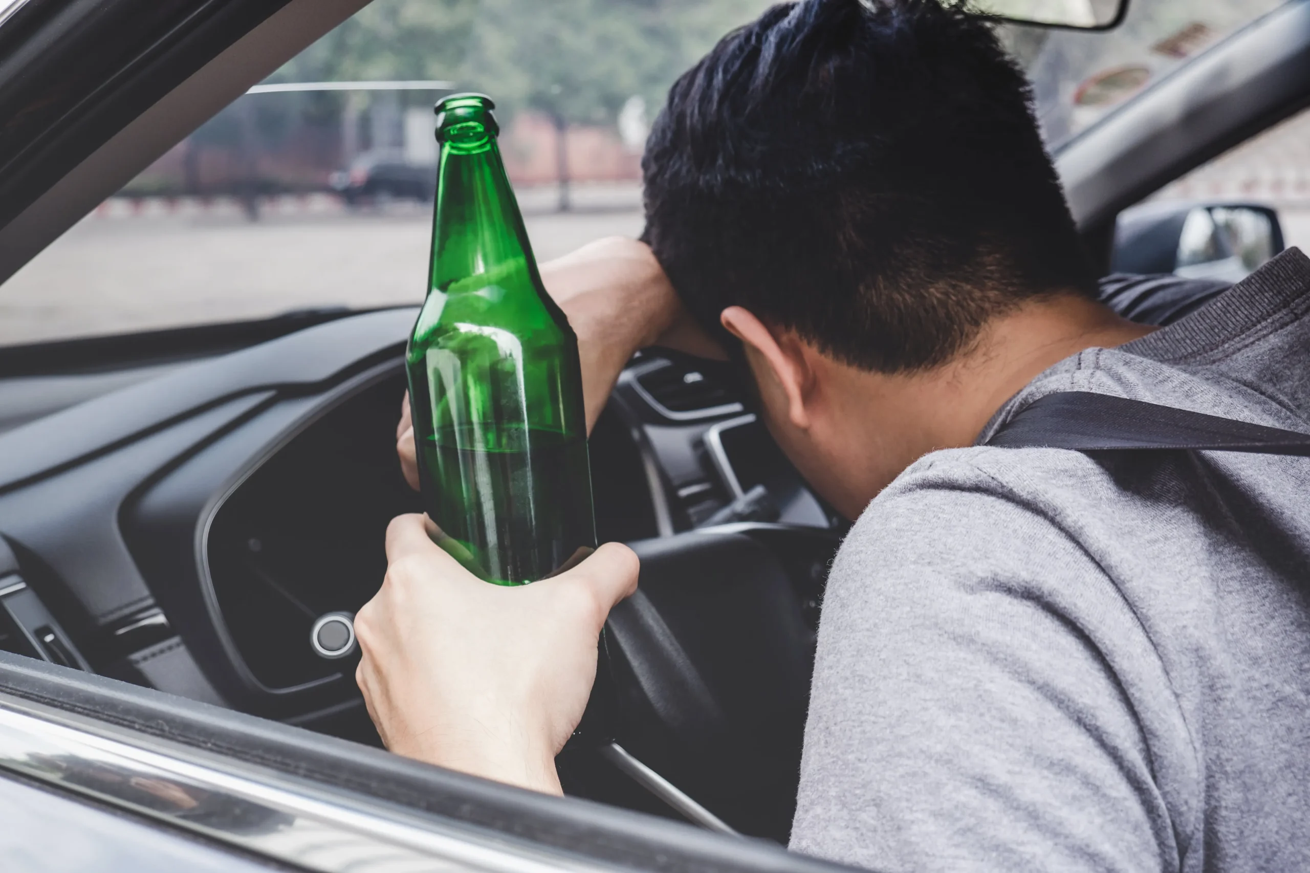 A person driving drunk, holding a green beer bottle.