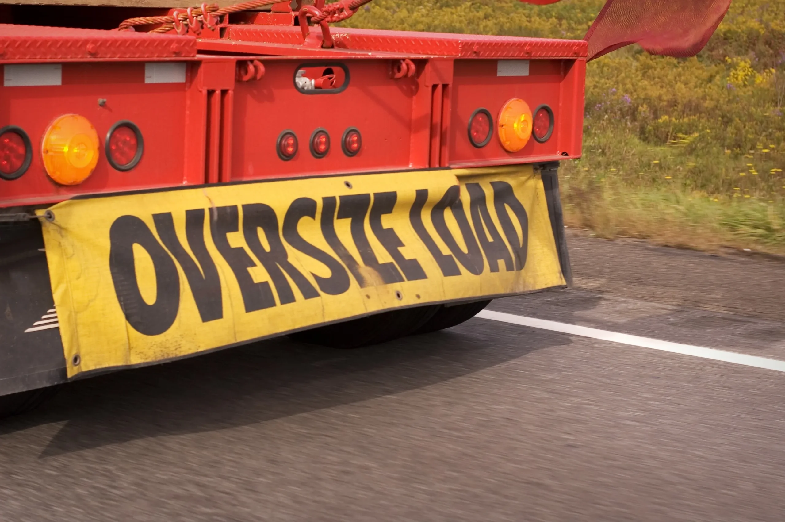 A red truck with a yellow sign warning about an oversized load.