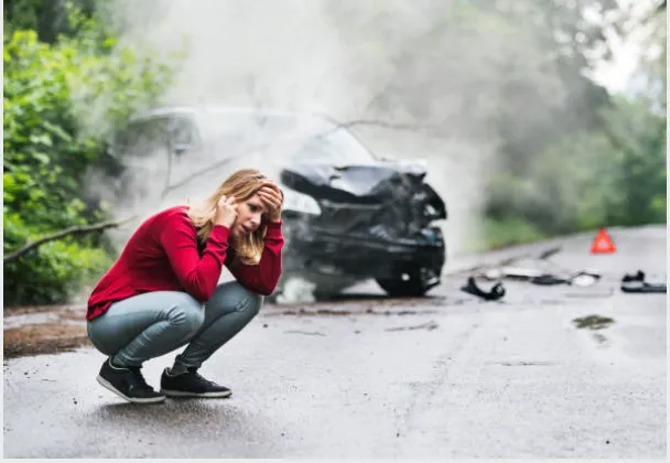 A person crouched down,  talking on the phone after a car accident.