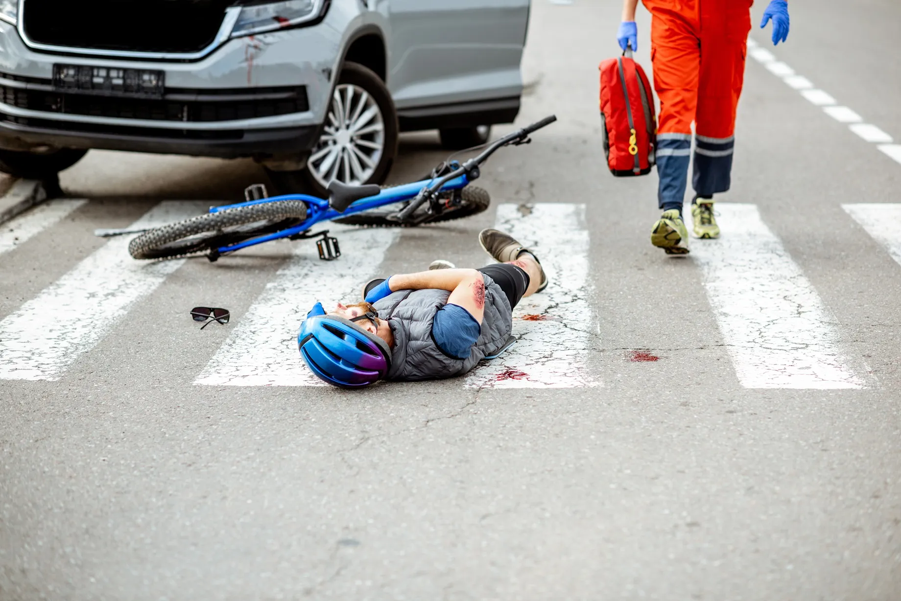 A cyclist laying in the crosswalk after being hit by a car.